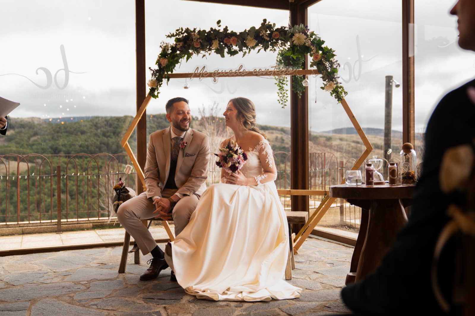 Novios sentados sonriendo bajo un arco floral